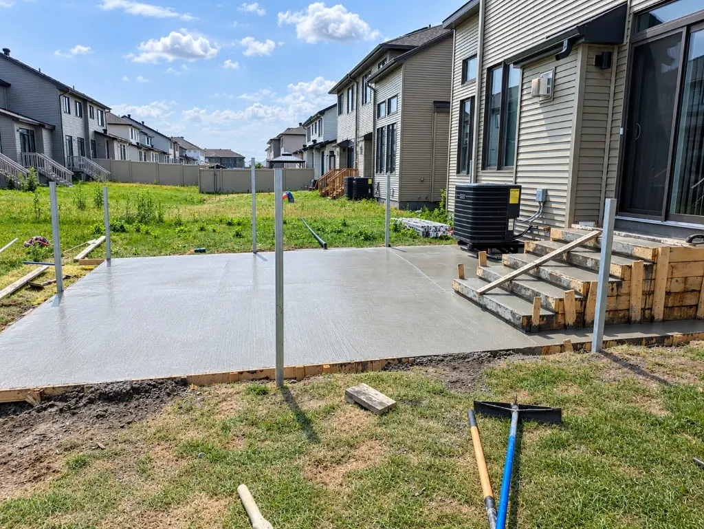 Freshly poured backyard concrete pad with wooden forms for steps up to the patio door