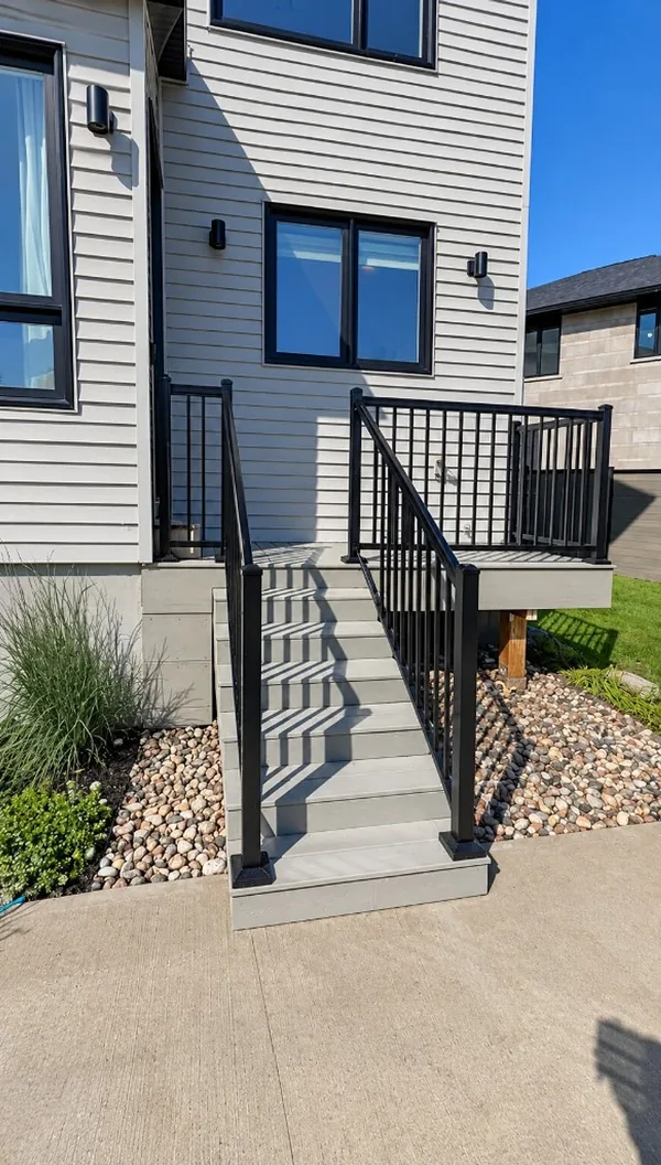 Grey composite steps and landing with black aluminum railings, edged with river rock