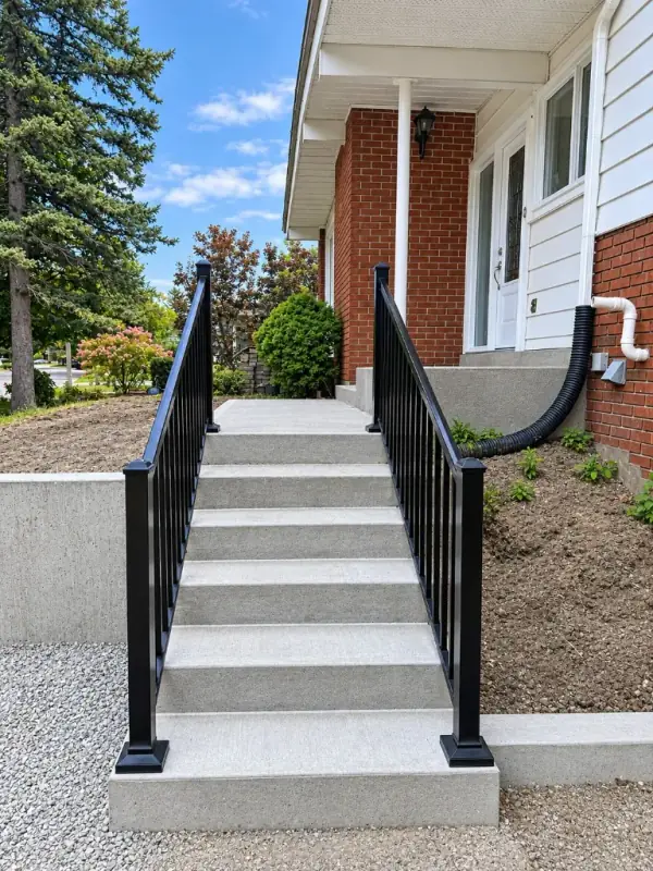 New concrete front steps with black aluminum railings beside a concrete retaining wall