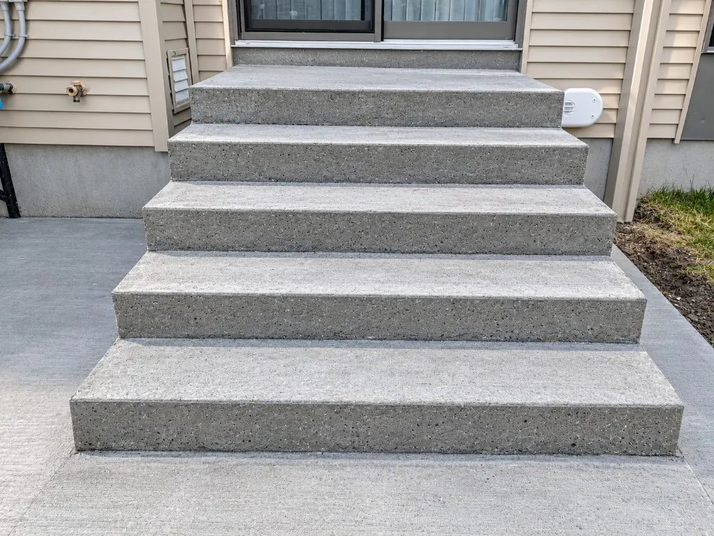 Five-riser concrete steps up to a patio door, over a new concrete pad