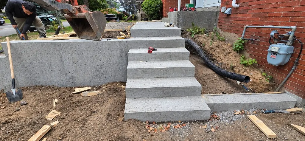 New concrete steps and wall during construction, with drainage pipe laid beside the house
