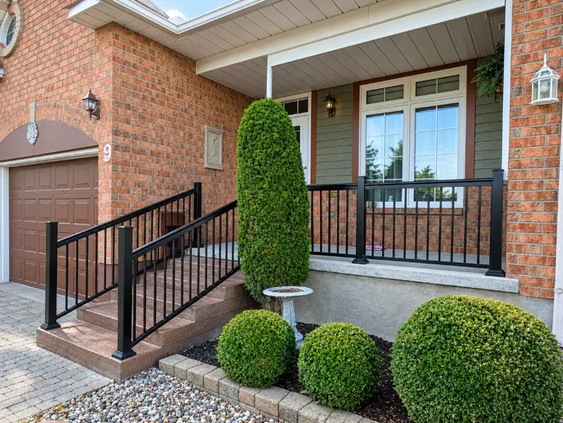 Front steps and porch with black aluminum railings and landscaping