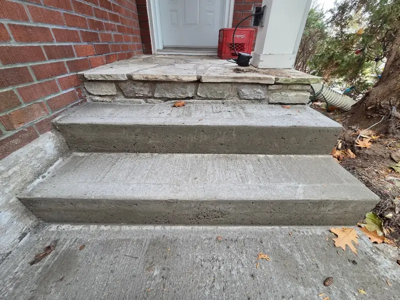 New two-riser concrete steps below a flagstone landing at a brick house