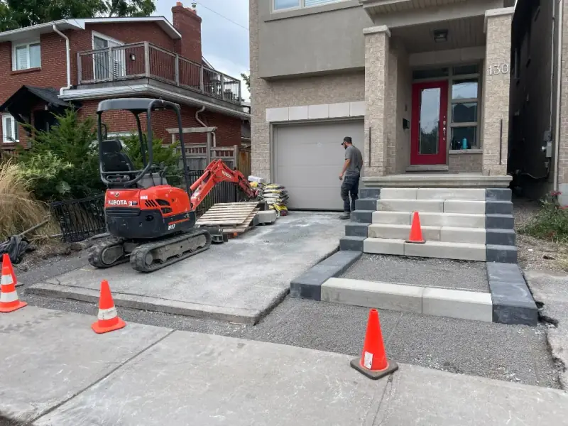 Crew building new stone-slab front steps and a walkway, with a mini excavator on site