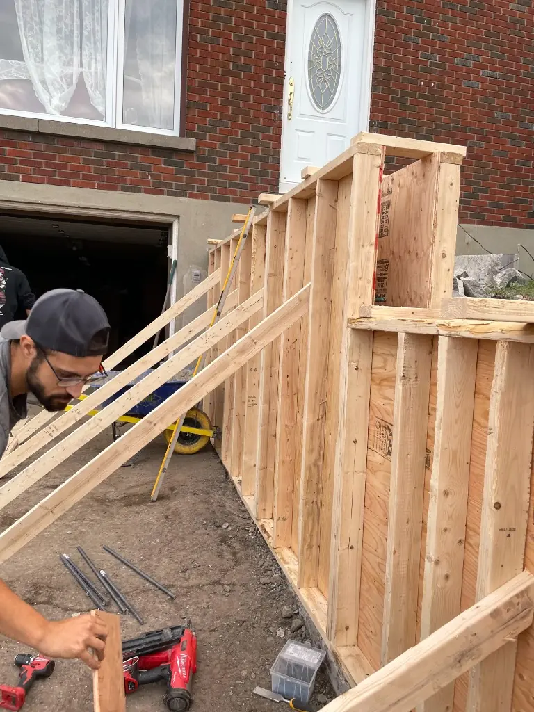 Crew member building tall wooden forms for a concrete wall and steps