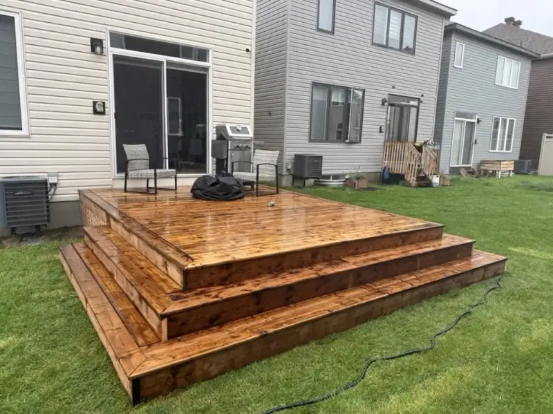 Stained wood deck with steps wrapping around two sides, in a backyard